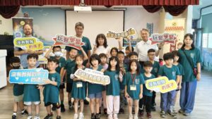 瑞平國小學生與師長在兒童傷害預防課程中合影，手持玩聚學習與教育公益標語