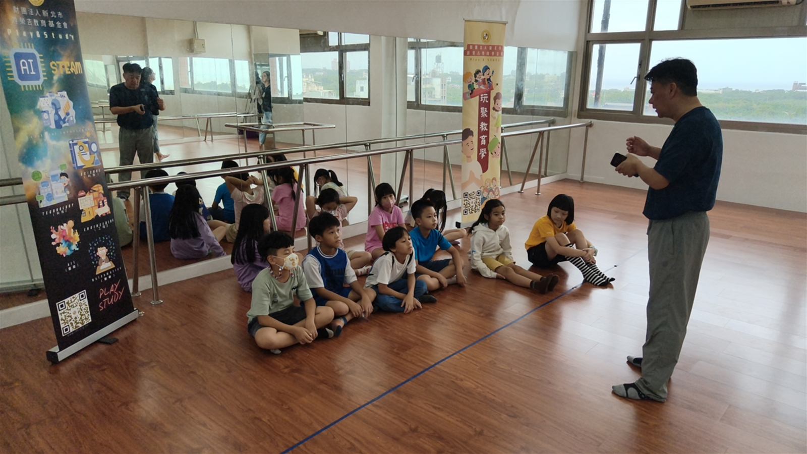師長在舞蹈教室中向興仁國小學生說明兒童音樂劇課程,孩子席地聆聽