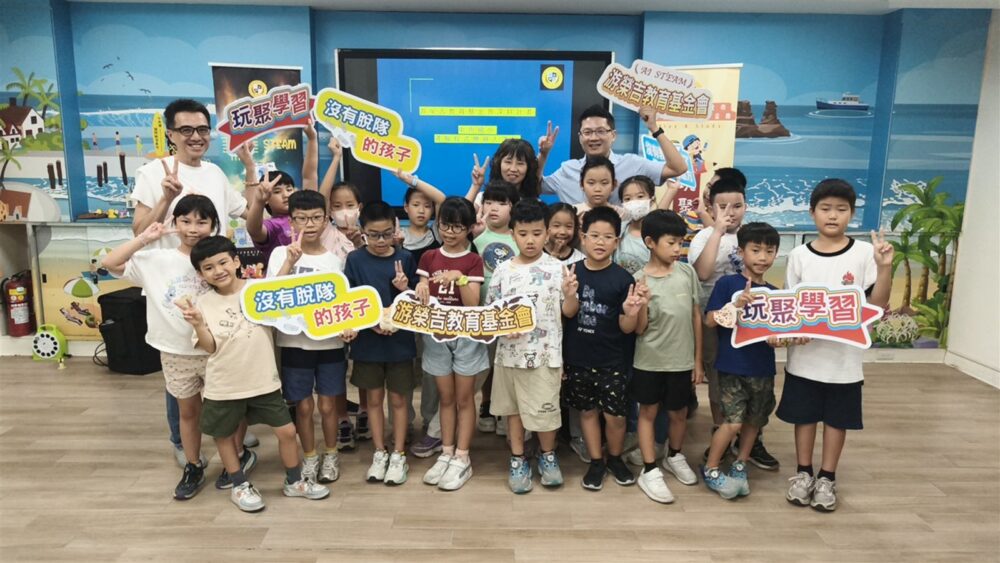 中角國小學生與師長在邏輯程式教育機器人課程始業式合影，手持玩聚學習標語