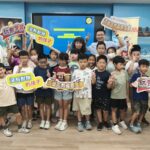 中角國小學生與師長在邏輯程式教育機器人課程始業式合影，手持玩聚學習標語