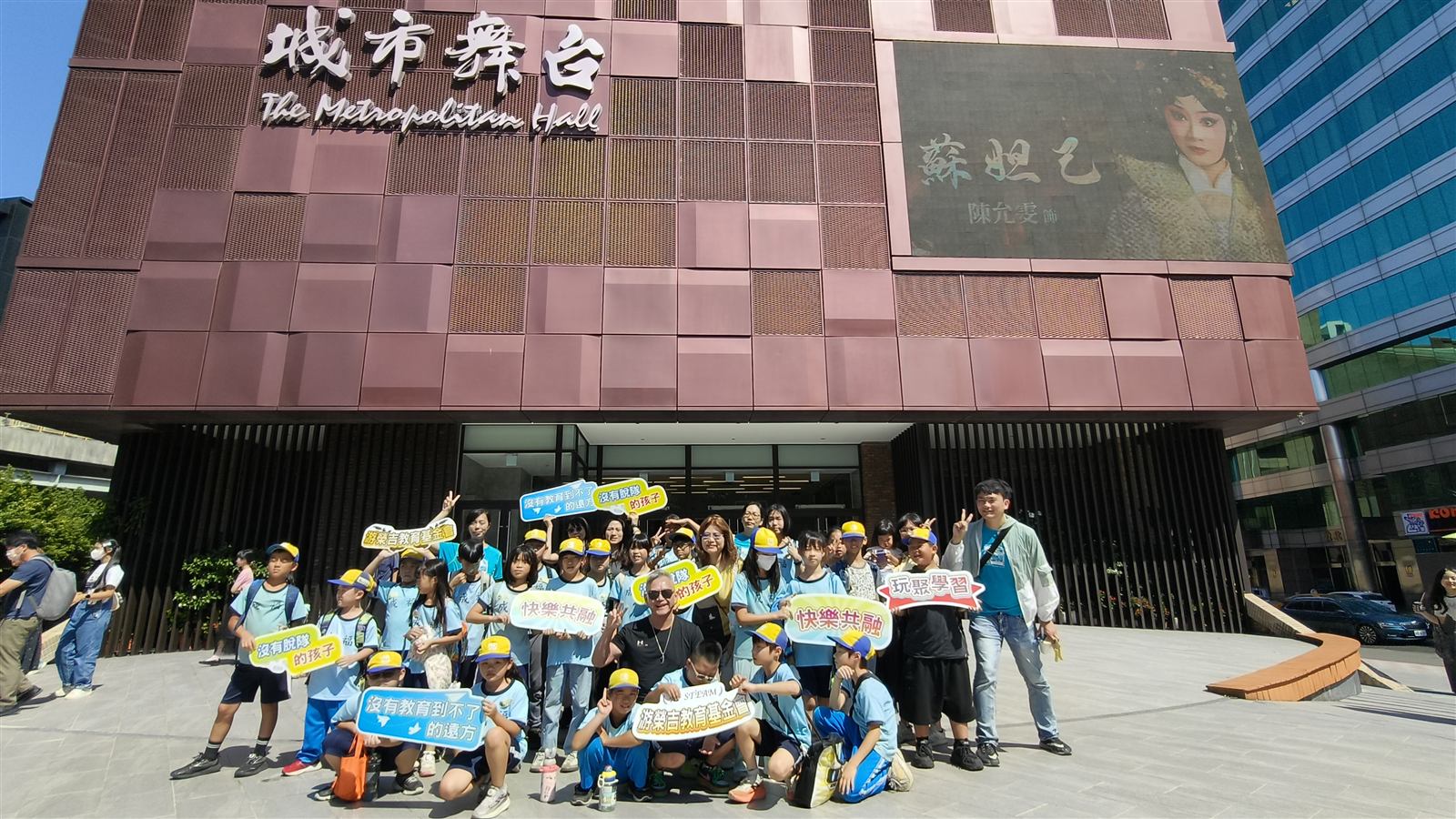 學生與師長手持玩聚學習看板在城市舞台前合影