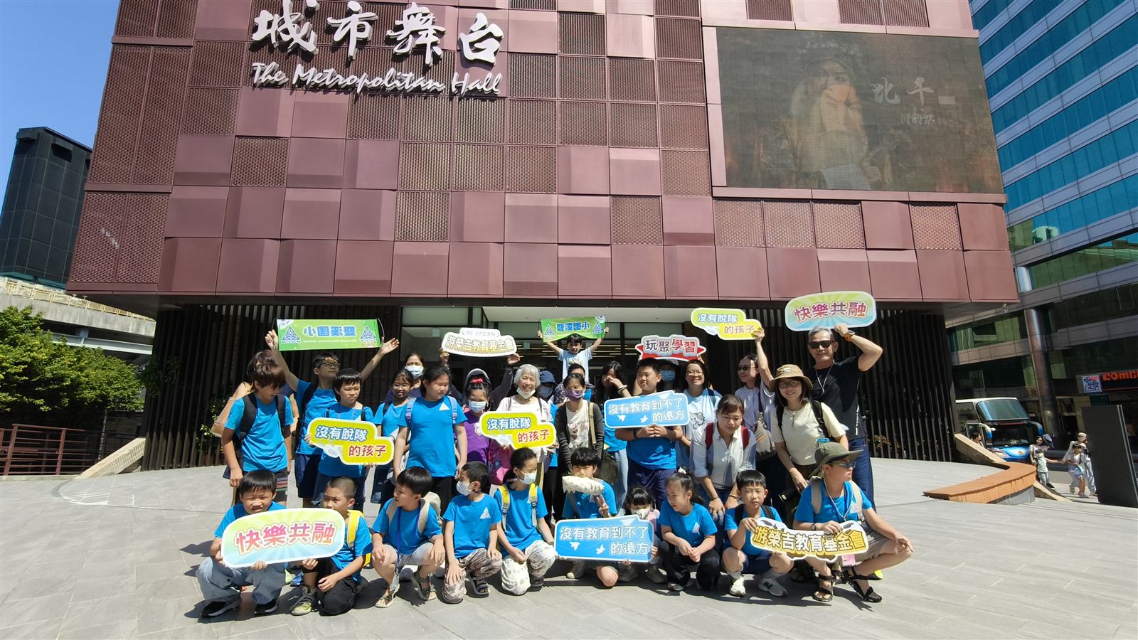 穿著藍色上衣的學生與師長在城市舞台前合影